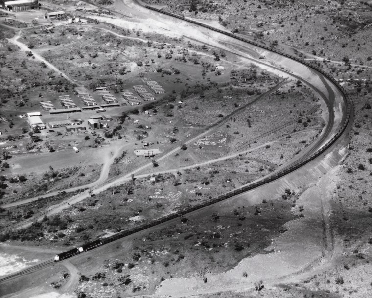 Aerial photograph of a train of 119 empty ore carriages passing the construction camp at Mt Tom